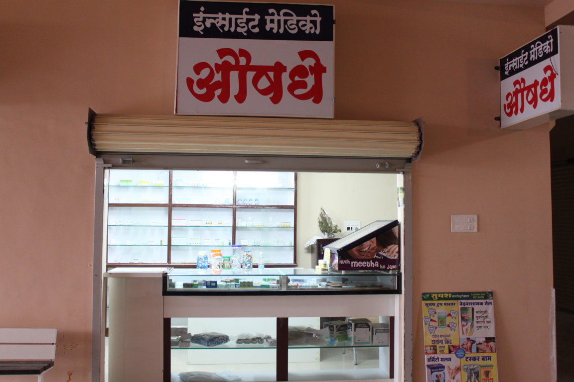 Insight Medico dispensing window viewed from the corridor at Insight Institute, with bilingual signage and back-shelf inventory visible inside
